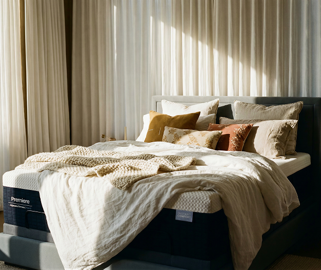 Bed with pillows and a blanket on a Premier mattress in a bright room with curtains.