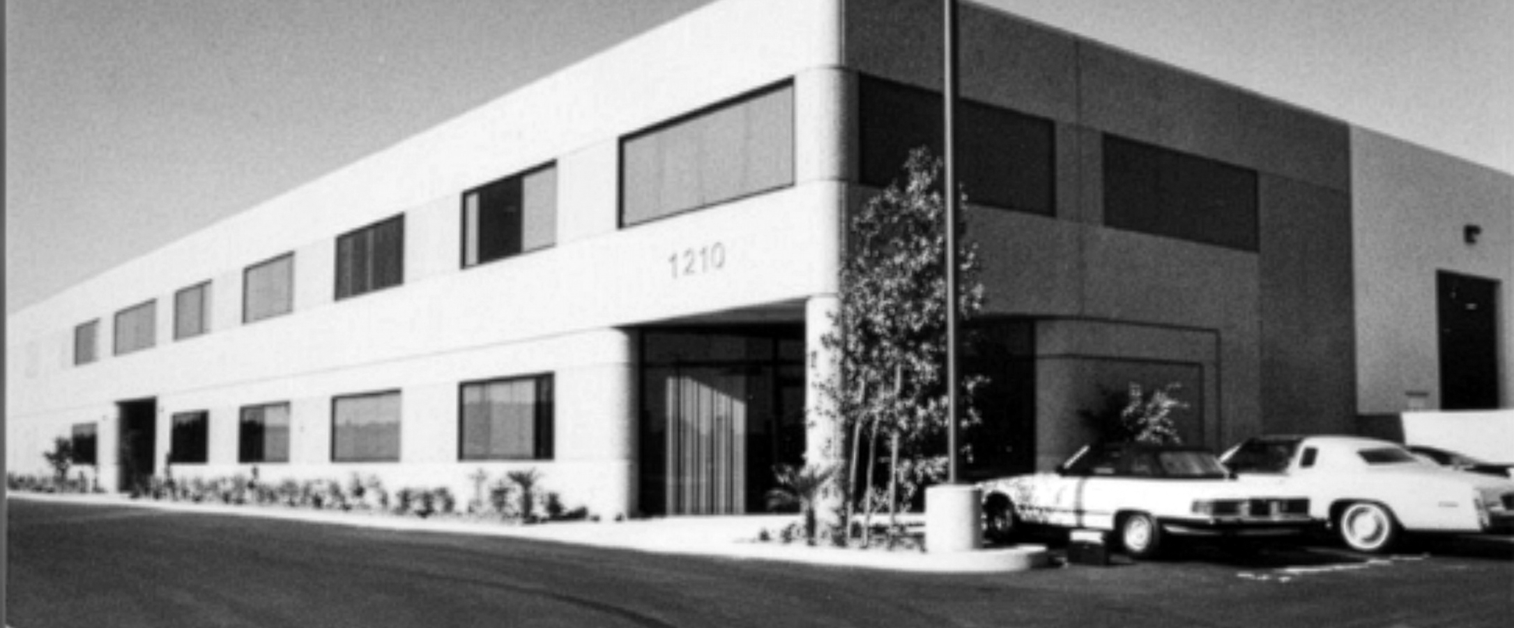 Black and white photo of a modern building with cars parked in front